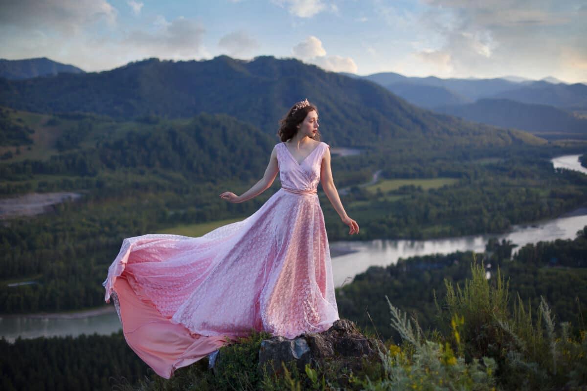 A girl in a pink dress with a long train. Bird's-eye. On the top of the mountain.