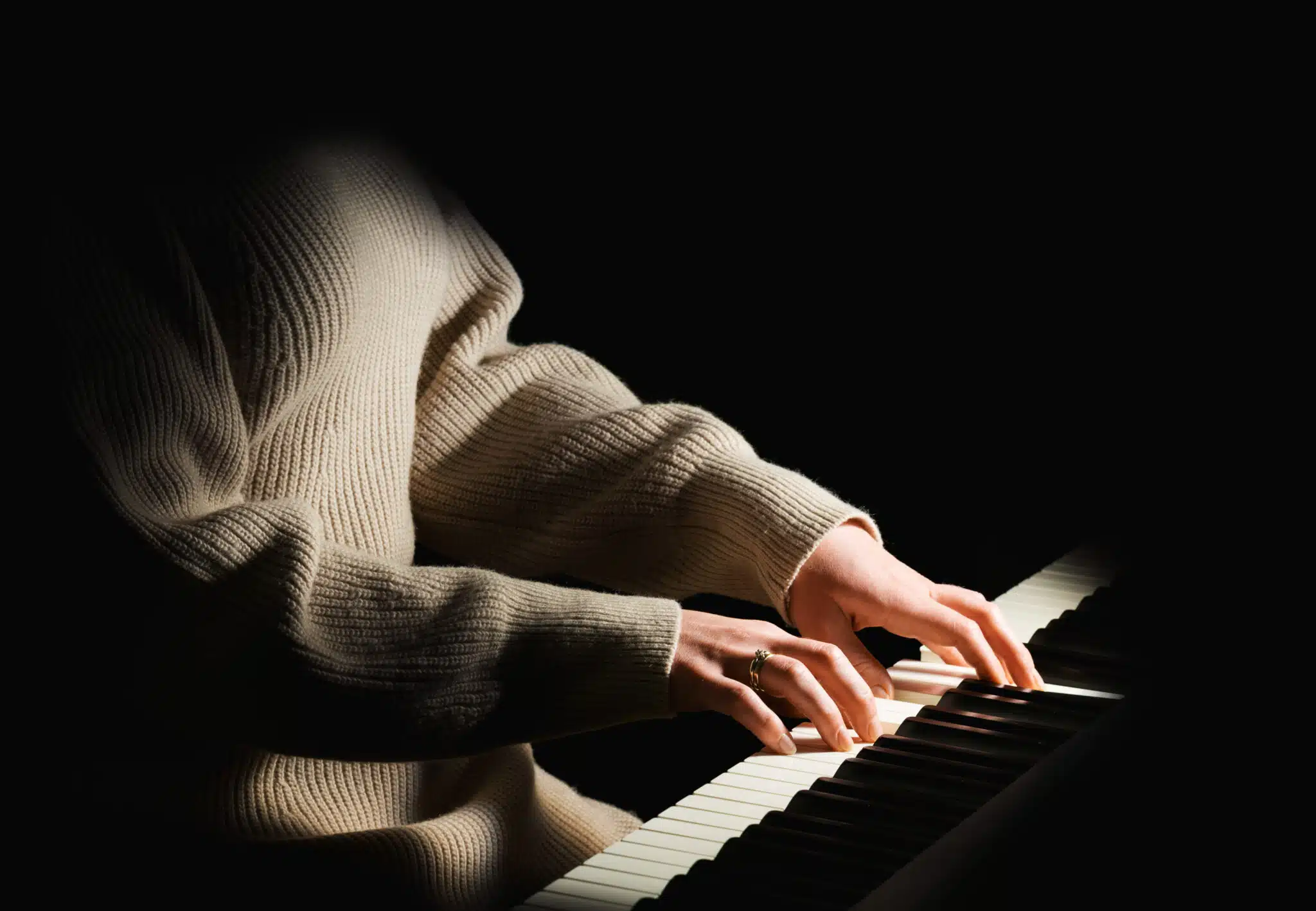 Female pianist in sweater dress plays chord on black piano 