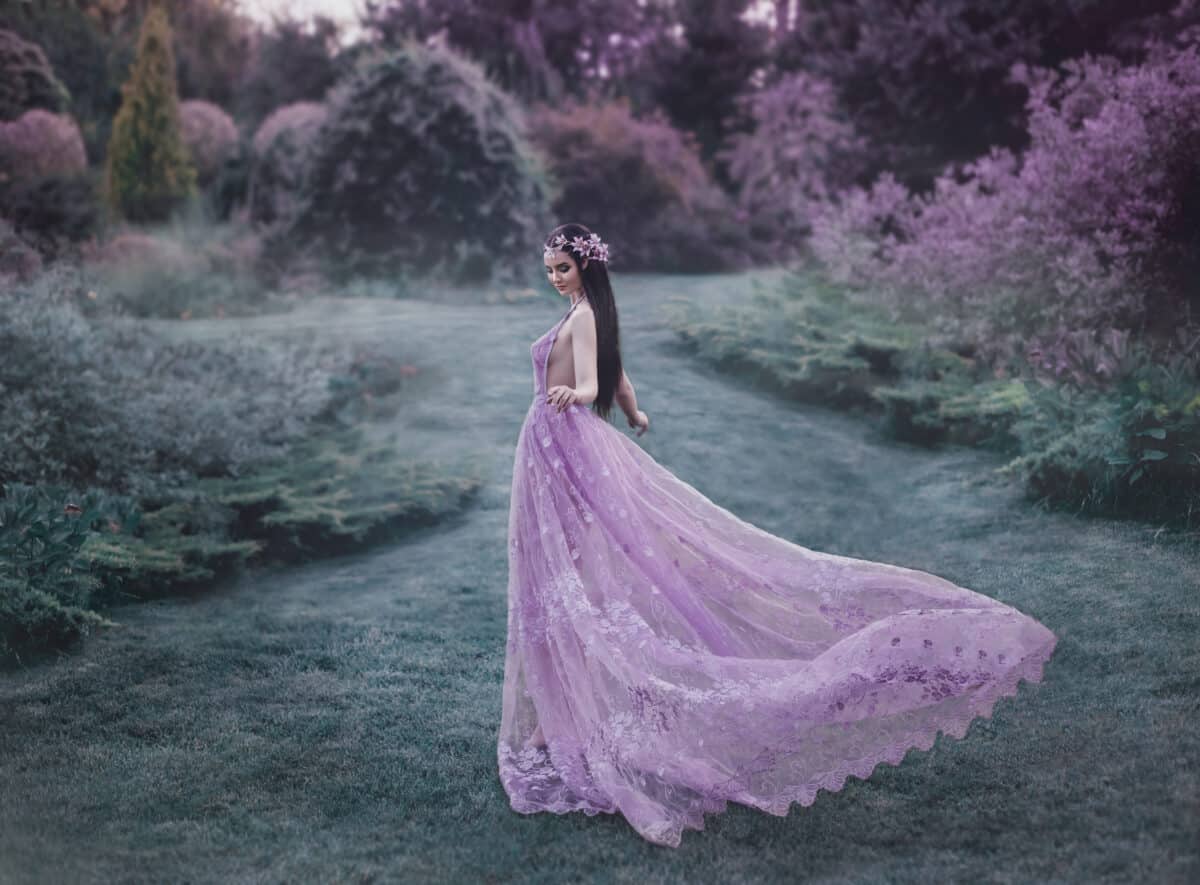 Fantasy girl in a fairy garden. Young elf in a beautiful purple dress with a long train.