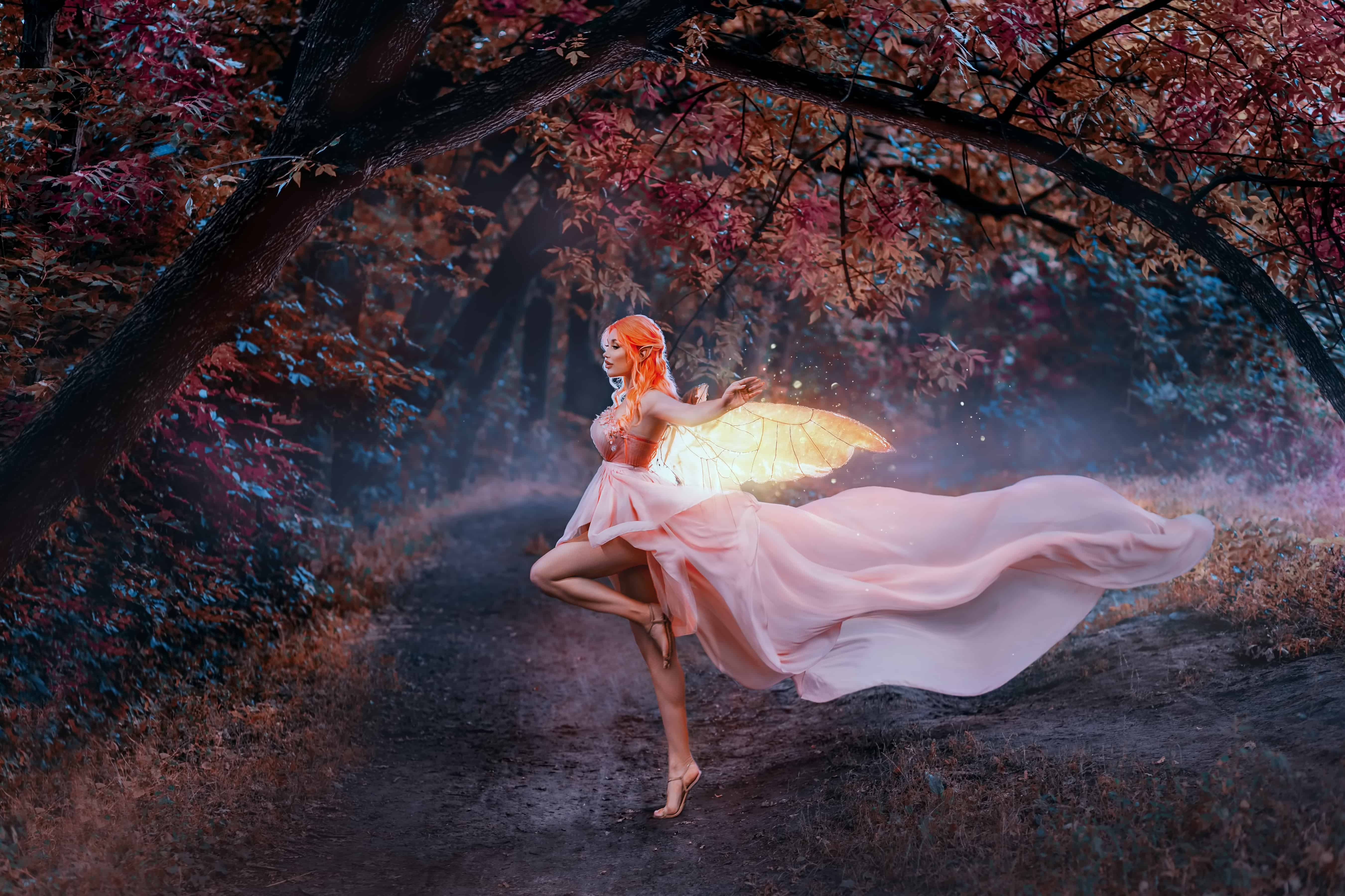 Portrait fantasy woman fairy, golden glowing butterfly wings. Pink dress silk train skirt waving fabric flies in wind. Night autumn forest orange trees. Sexy elf girl, red hair art creative clothes