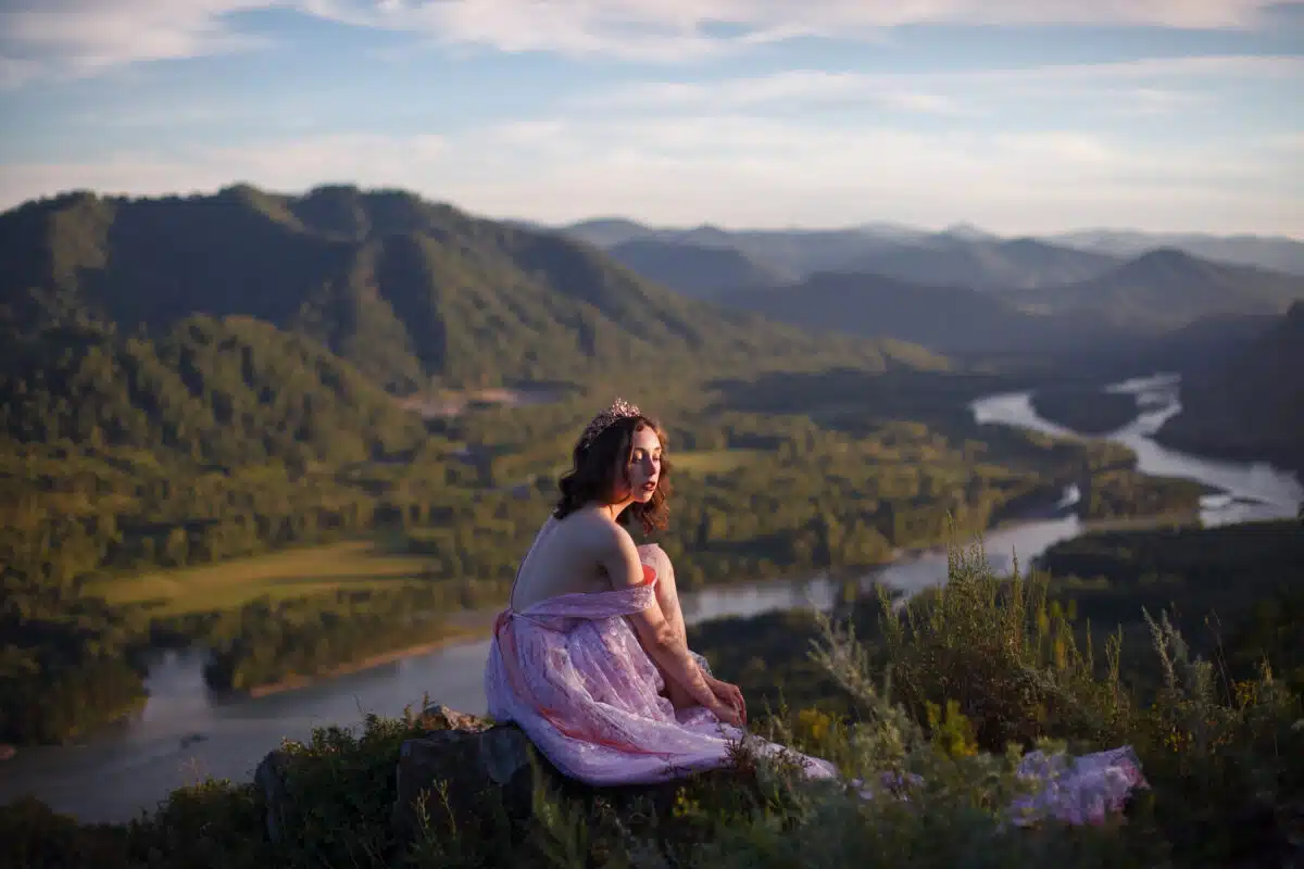 A girl in a pink dress with a long train. Bird's-eye. On the top of the mountain.
