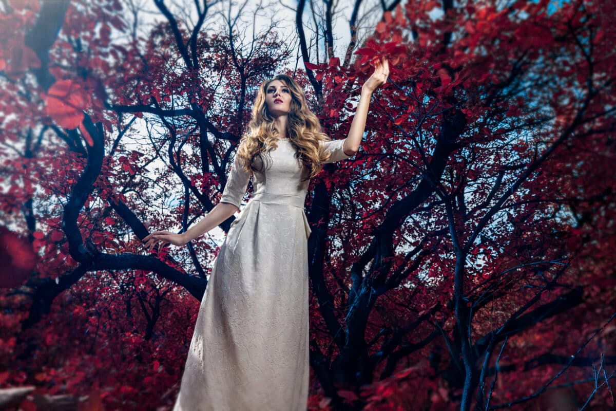Beautiful girl in white long dress in the fairytale autumn forest with red foliage like an enchantress. Fashion beauty and mystery concept