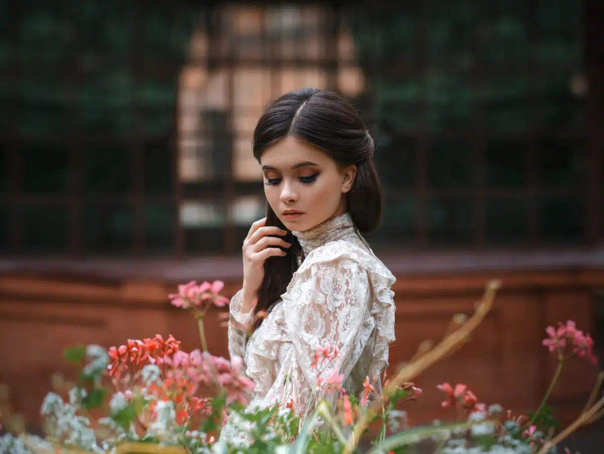 A girl walks in a flowering garden, she has a vintage blouse with a bow, chestnut long hair. she gently cares for her flowers. Sweetheart gardener. Artistic photography. Love of plants