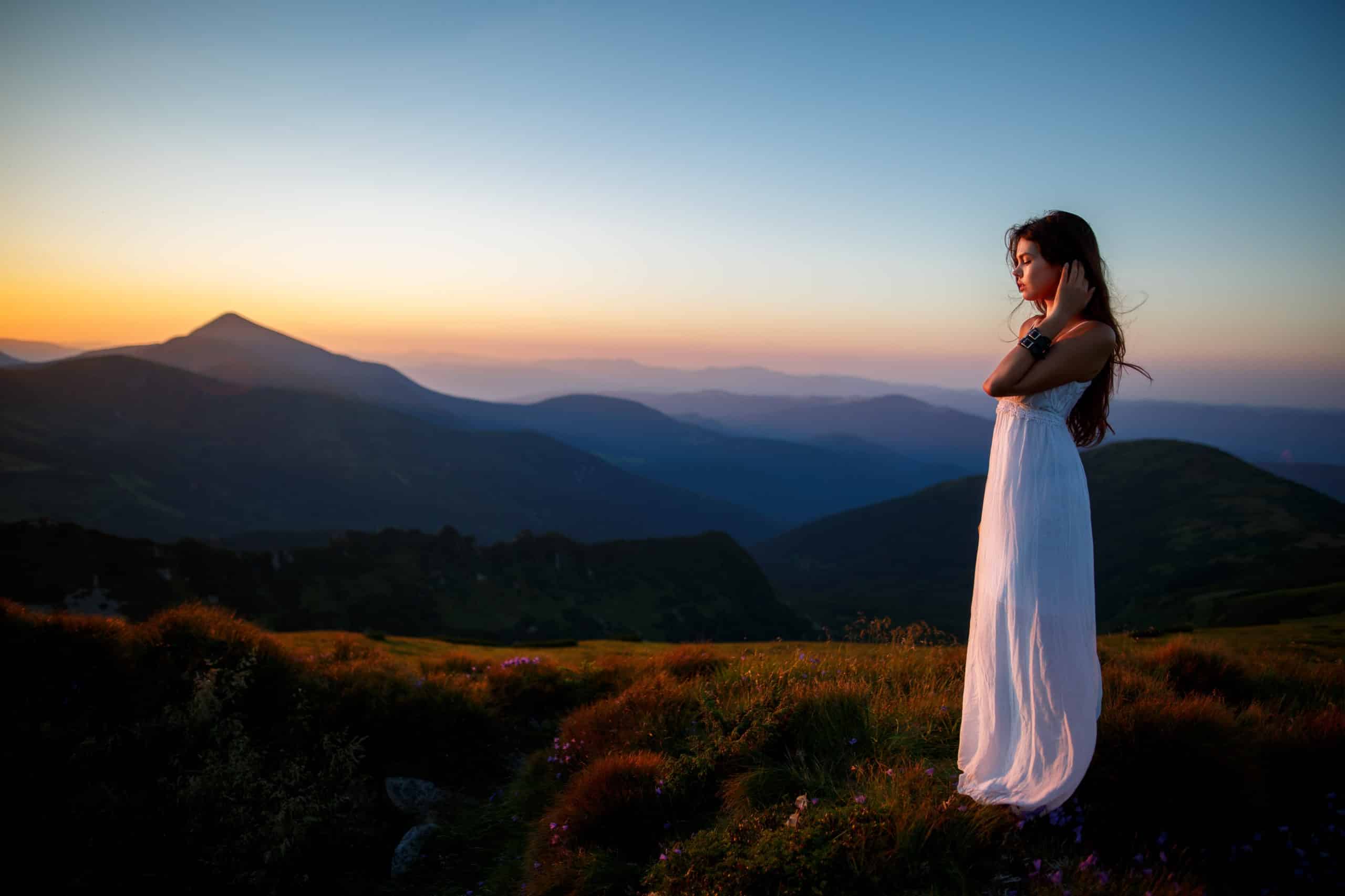 Young woman in long white dress on a hilltop enjoying the morning sunrise, nature.
