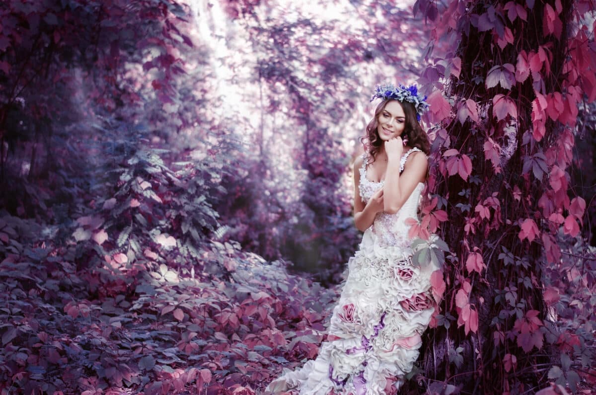 beautiful brown-haired woman in a long white dress, with a wreath of lavender on her head, is in the fairy forest