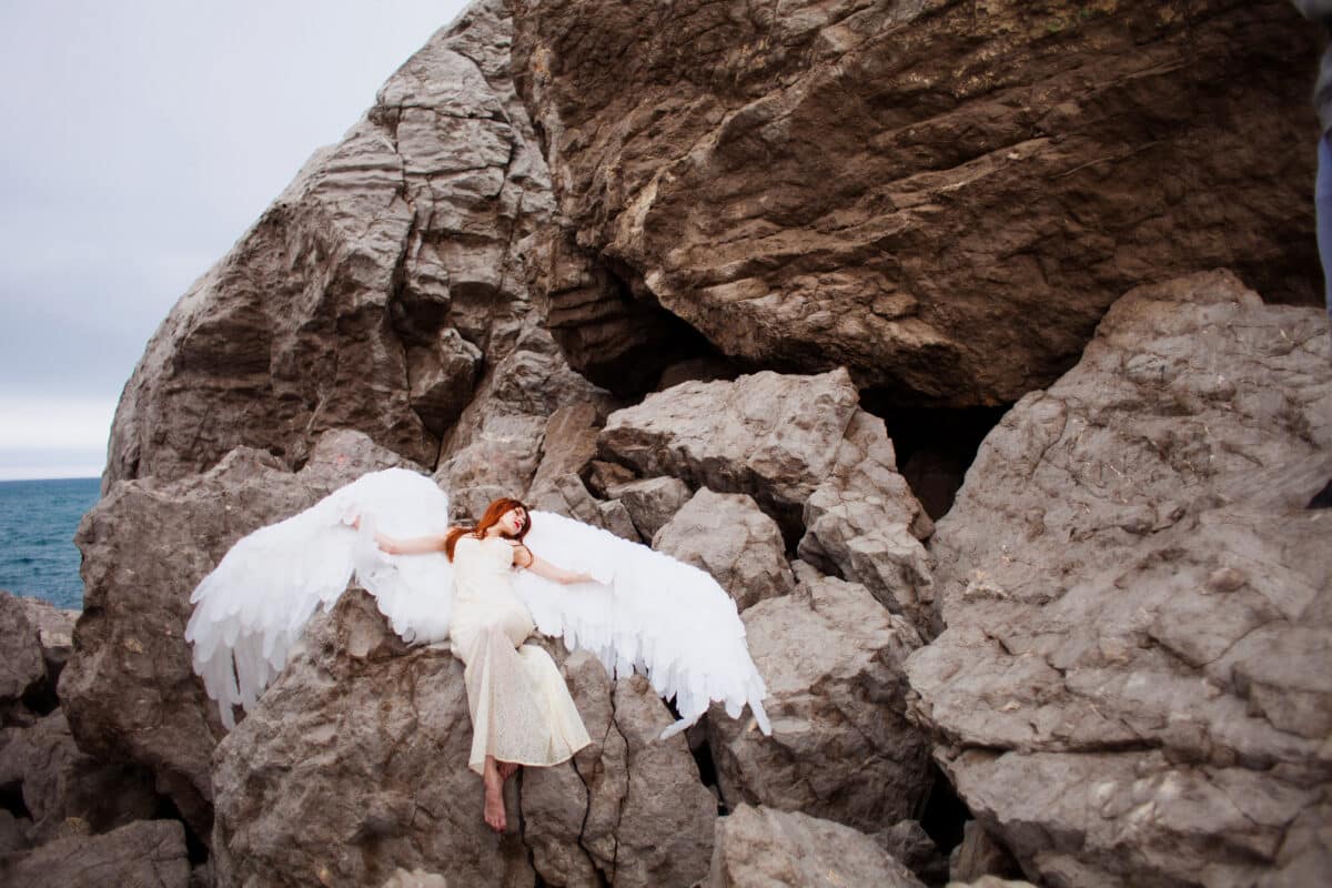 woman with white wings on a rock by the sea