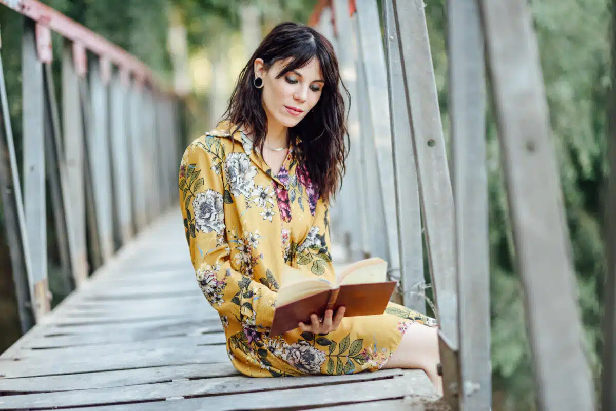 Young woman reading a book on a rural bridge.