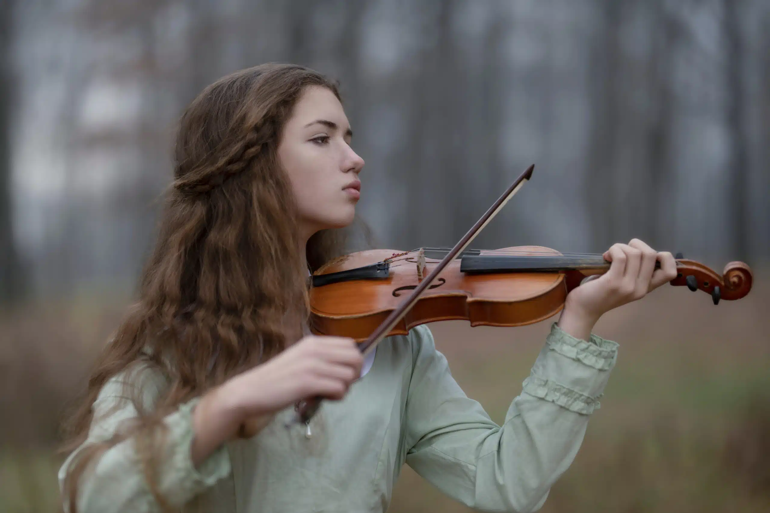 Young lady thoughtfully plays the violin in the autumn forest