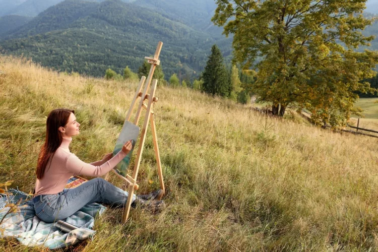 Young woman drawing landscape with soft pastels in nature. 