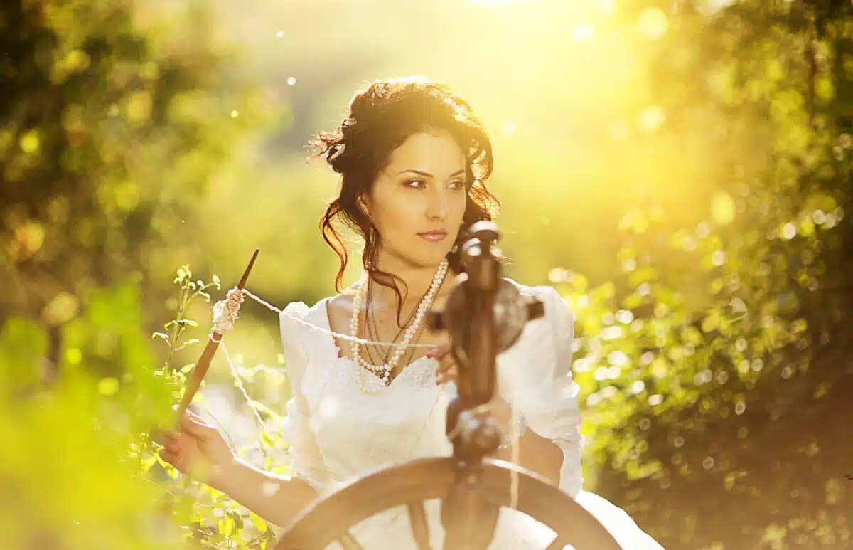 a lady dressed in white is working on her spinning wheel in the garden