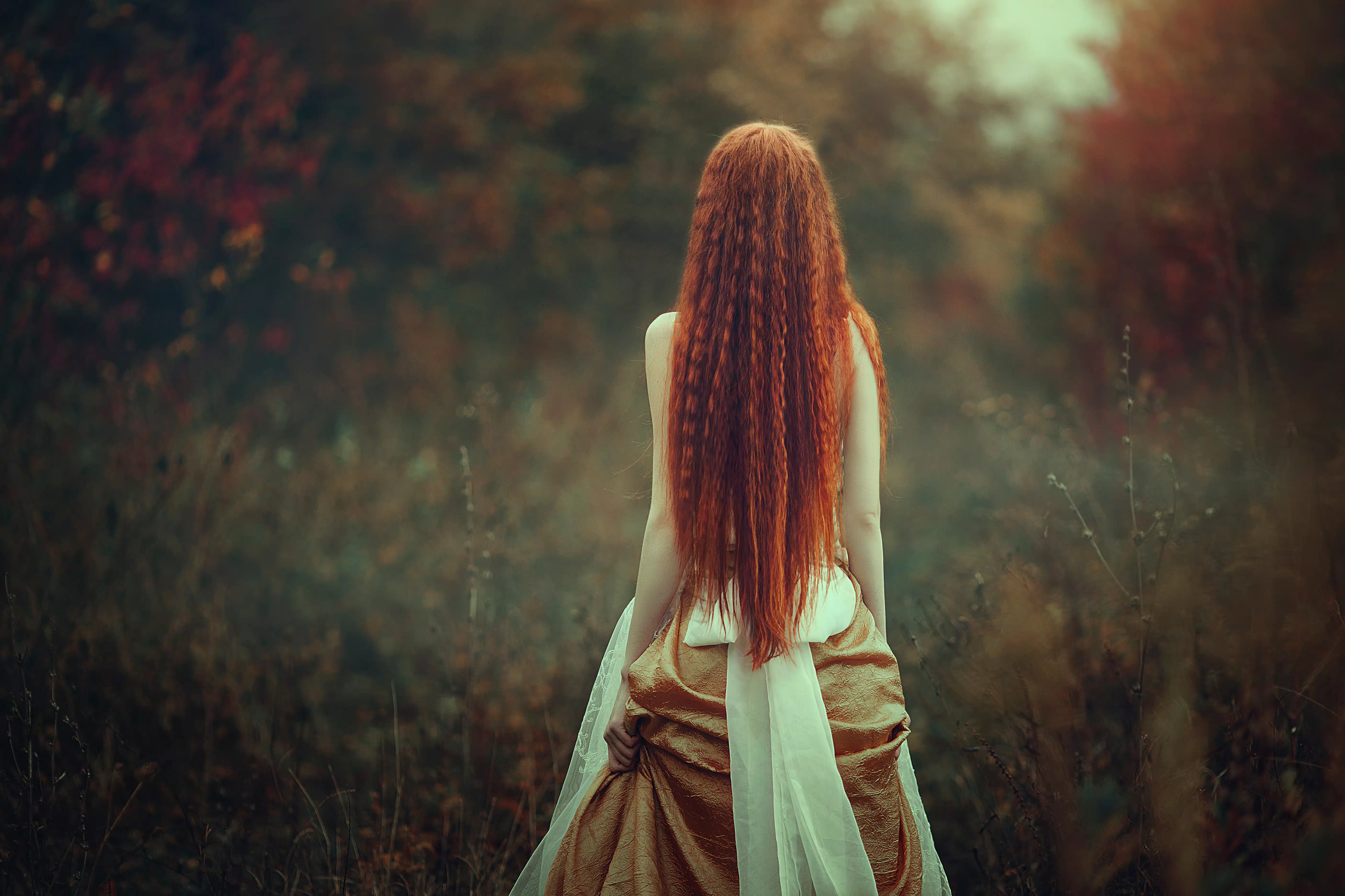 a young woman with very long red hair walks through the autumn forest