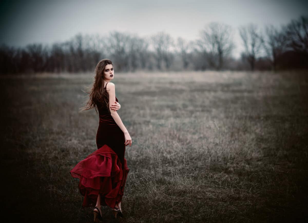 A beautiful sad lady in a red black dress in the field