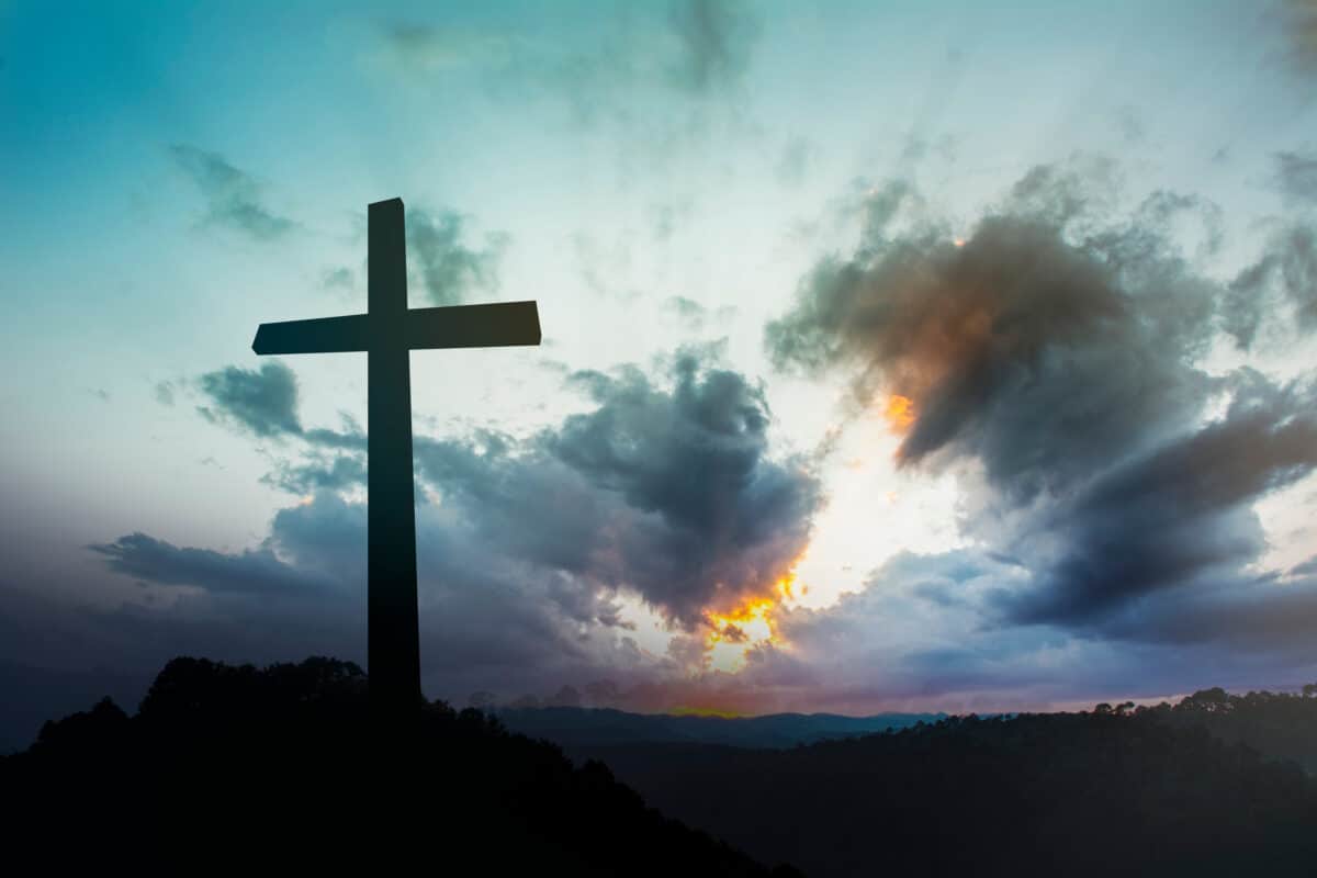 a black cross standing with gray and orange clouds in the background