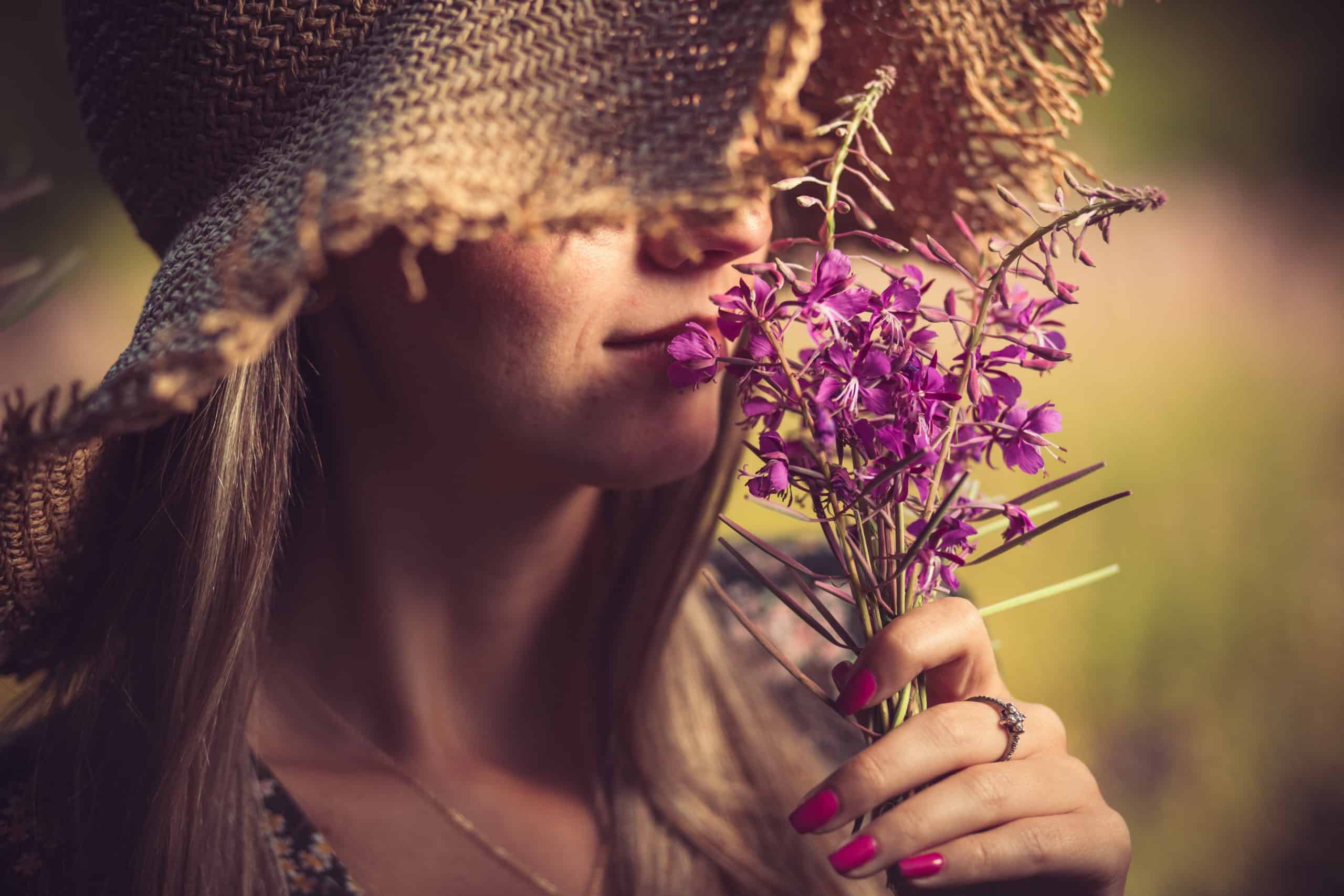 Young woman with summer hat, smelling purple flowers