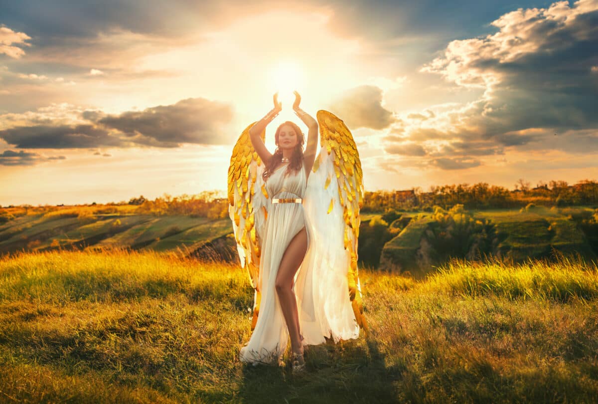 fantasy woman angel raises hands to blue dramatic sky with divine light on the mountain