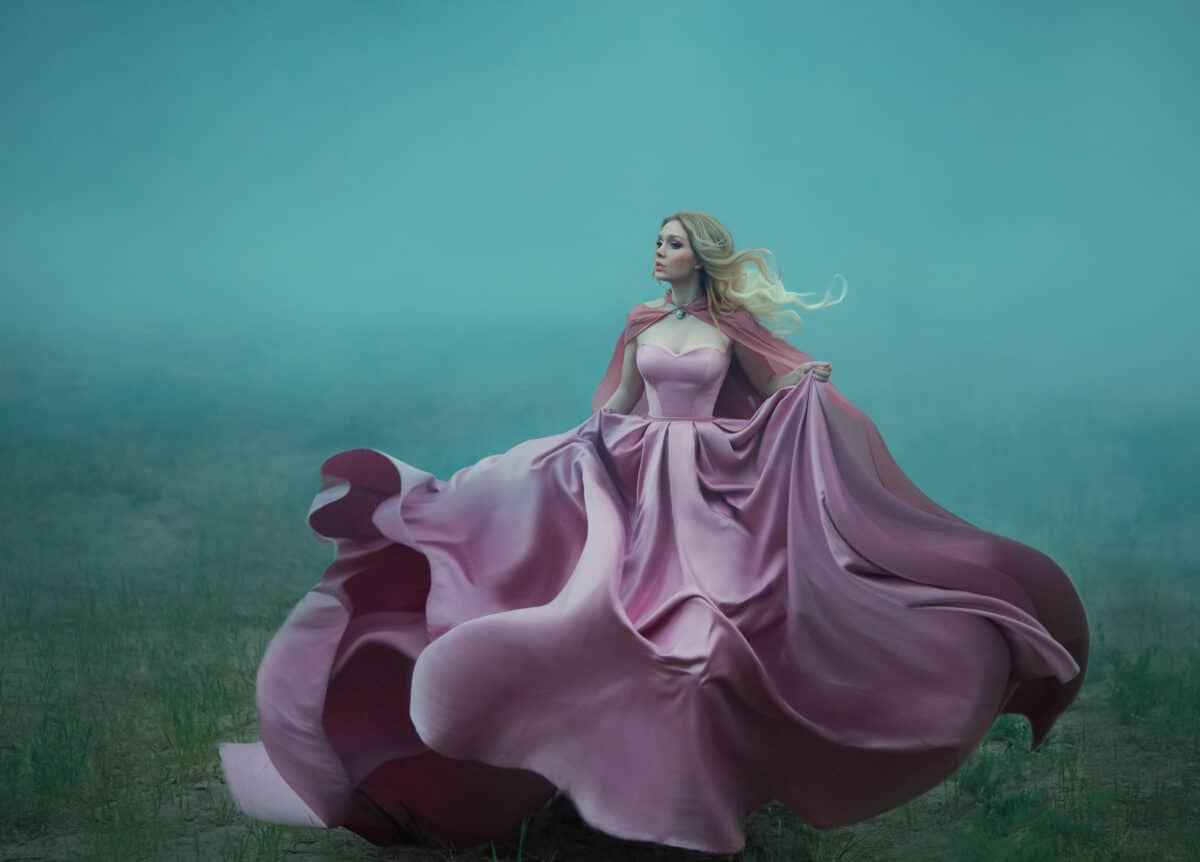Fantasy woman blonde hair queen runs in fog summer green forest. Pink royal silk satin dress fluttering fly waving in wind motion Art photo. Scared Girl fairy tale beauty princess escape from reality