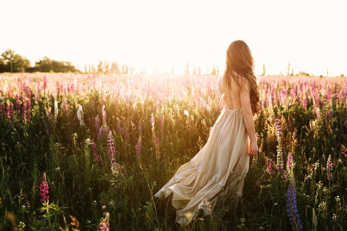 lady walks through the flowers in the field at sunset