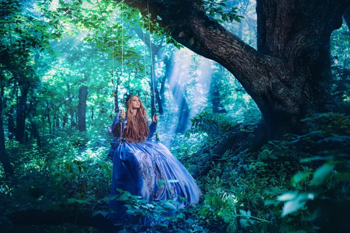 princess in a blue gown relaxing in a swing in the green forest