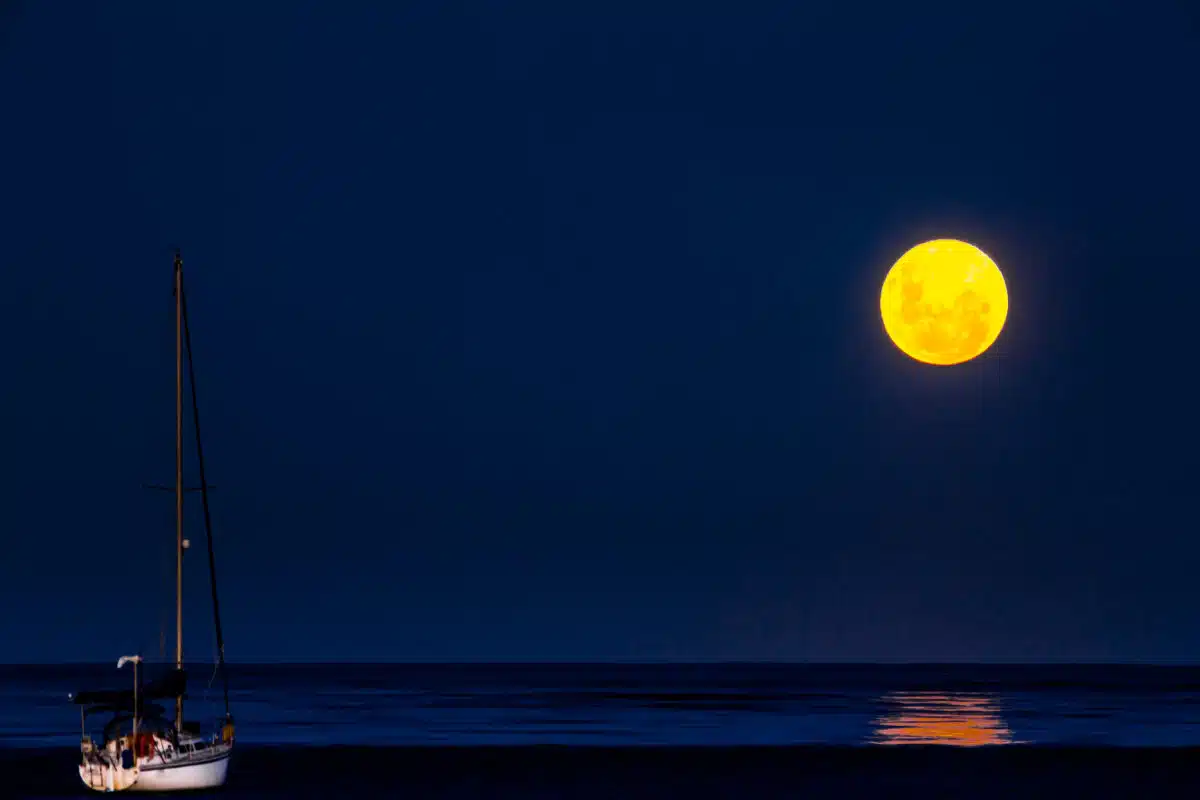 Full moonrise above sea with a sailboat in the foreground
