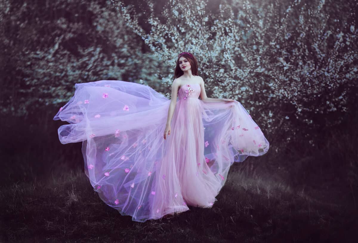Beautiful Romantic Girl with long hair in pink dress near flowering tree.