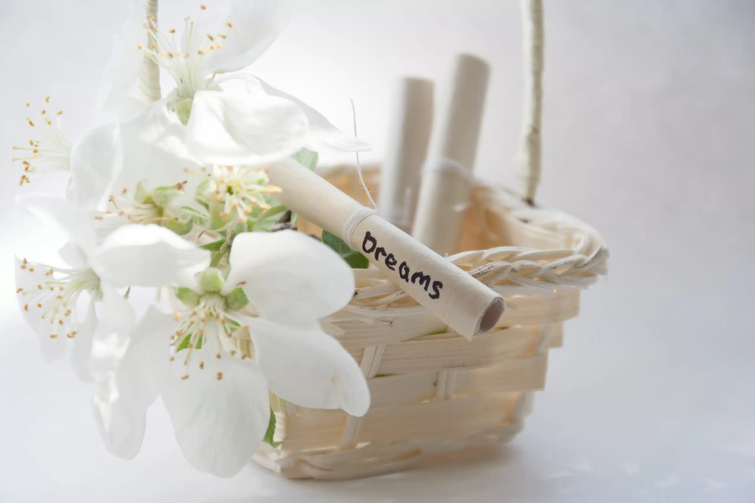 In a woven basket, white flowers and rolled paper with the word dream on it