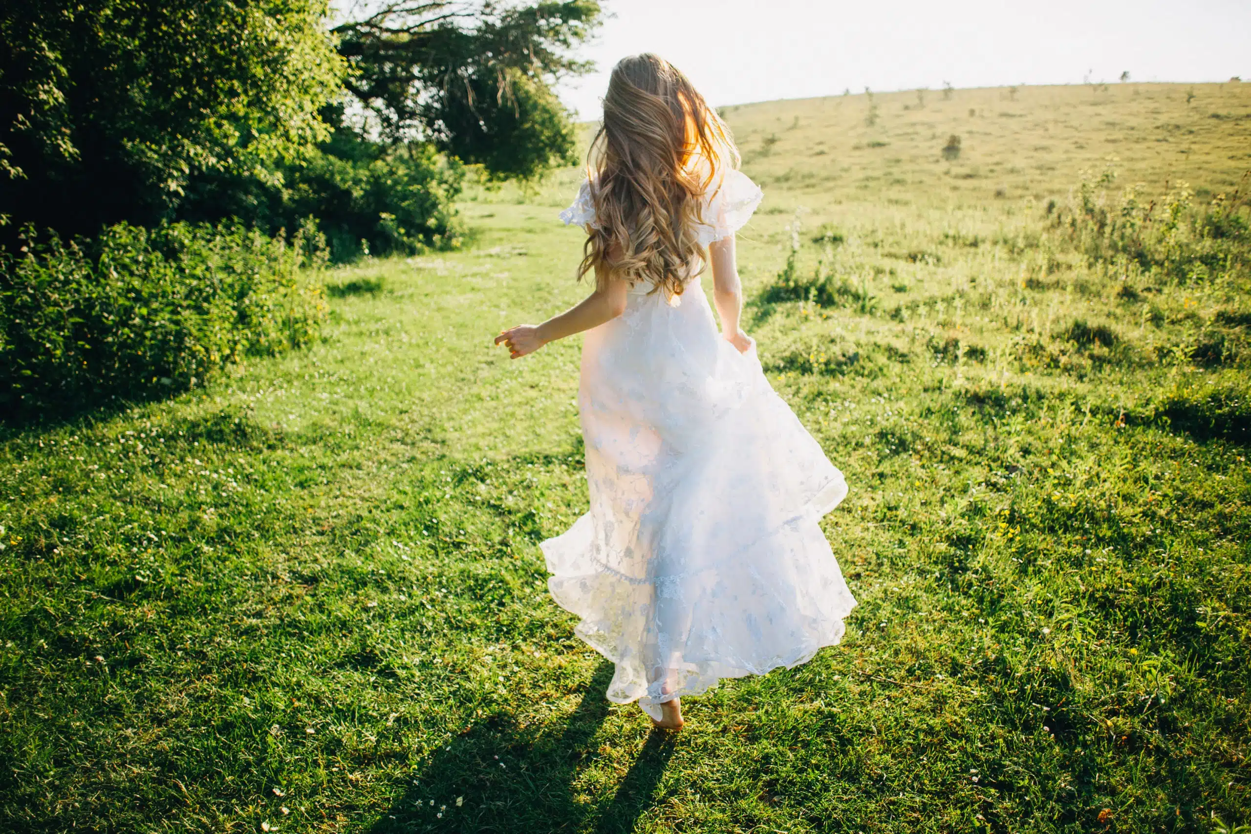 Young girl in a white dress in the meadow running away