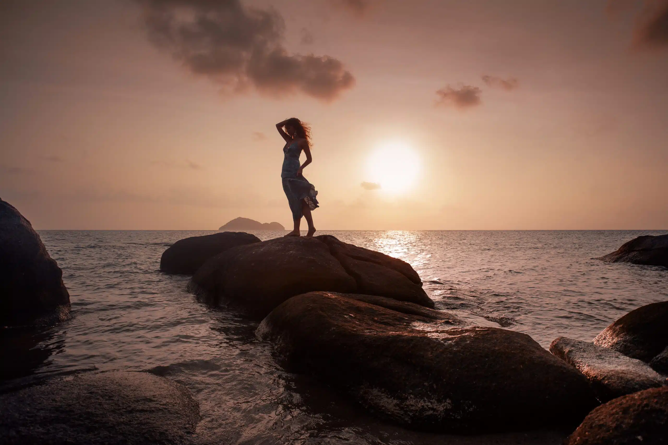silhoutte of a beautiful young woman standing on stone at sunset