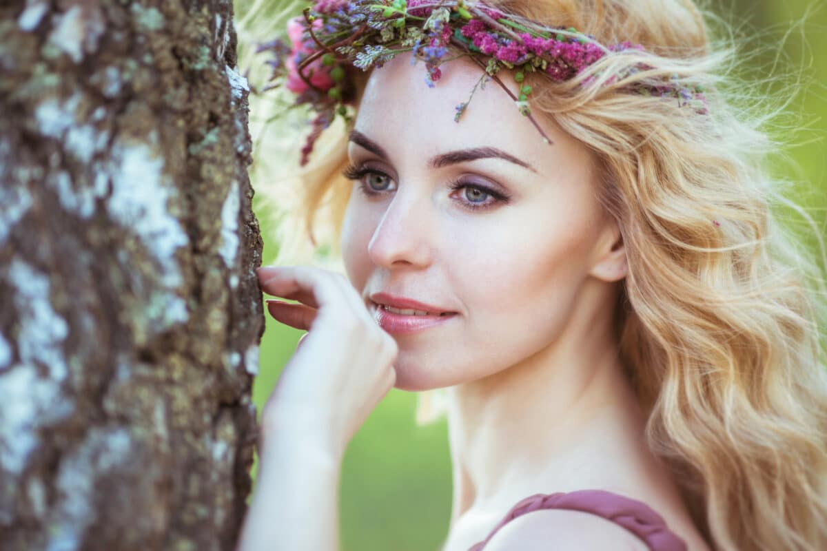 a charming blonde lady with a red flower head wreath in the woods