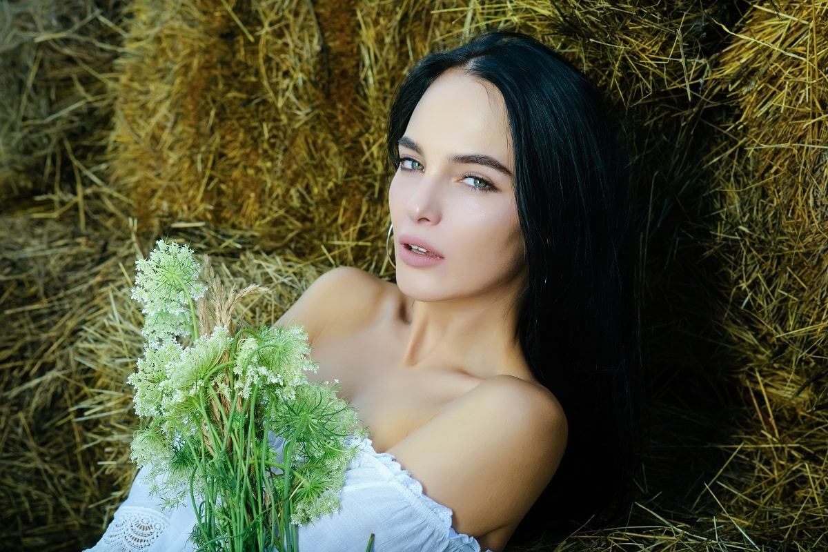 a pretty young woman outdoors relaxes on hay in a barn