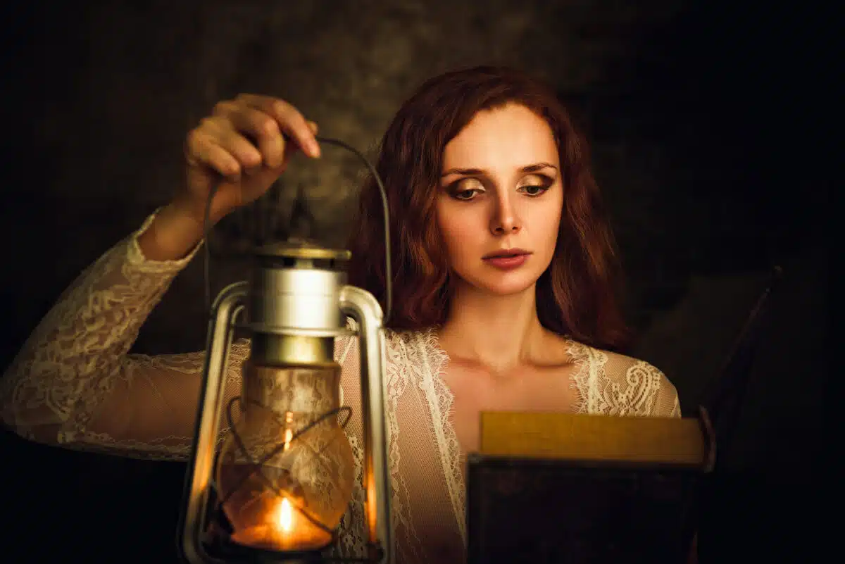 Beautiful red-haired young woman with a lamp reading a book