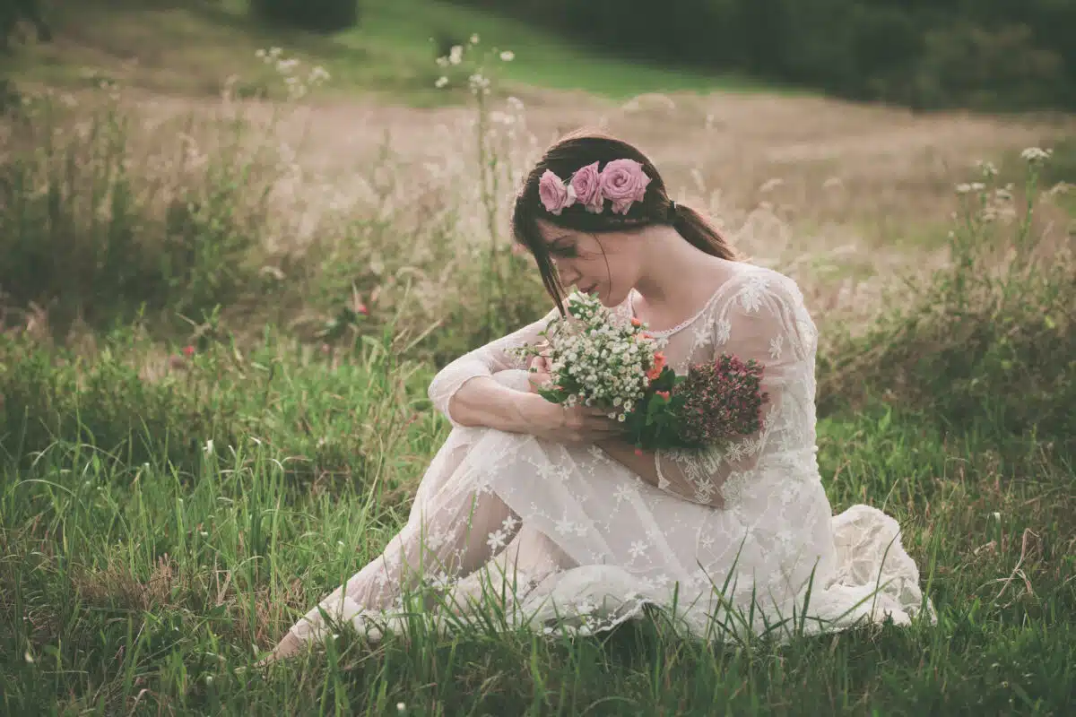 young beautiful lady in white lacy dress holds a bouquet of wild flowers on the meadow