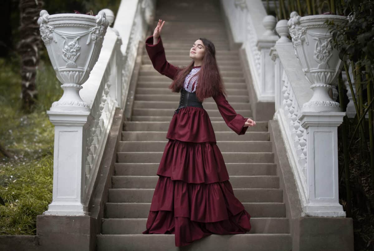 a princess in a burgundy dress on a beautiful white stone stairs