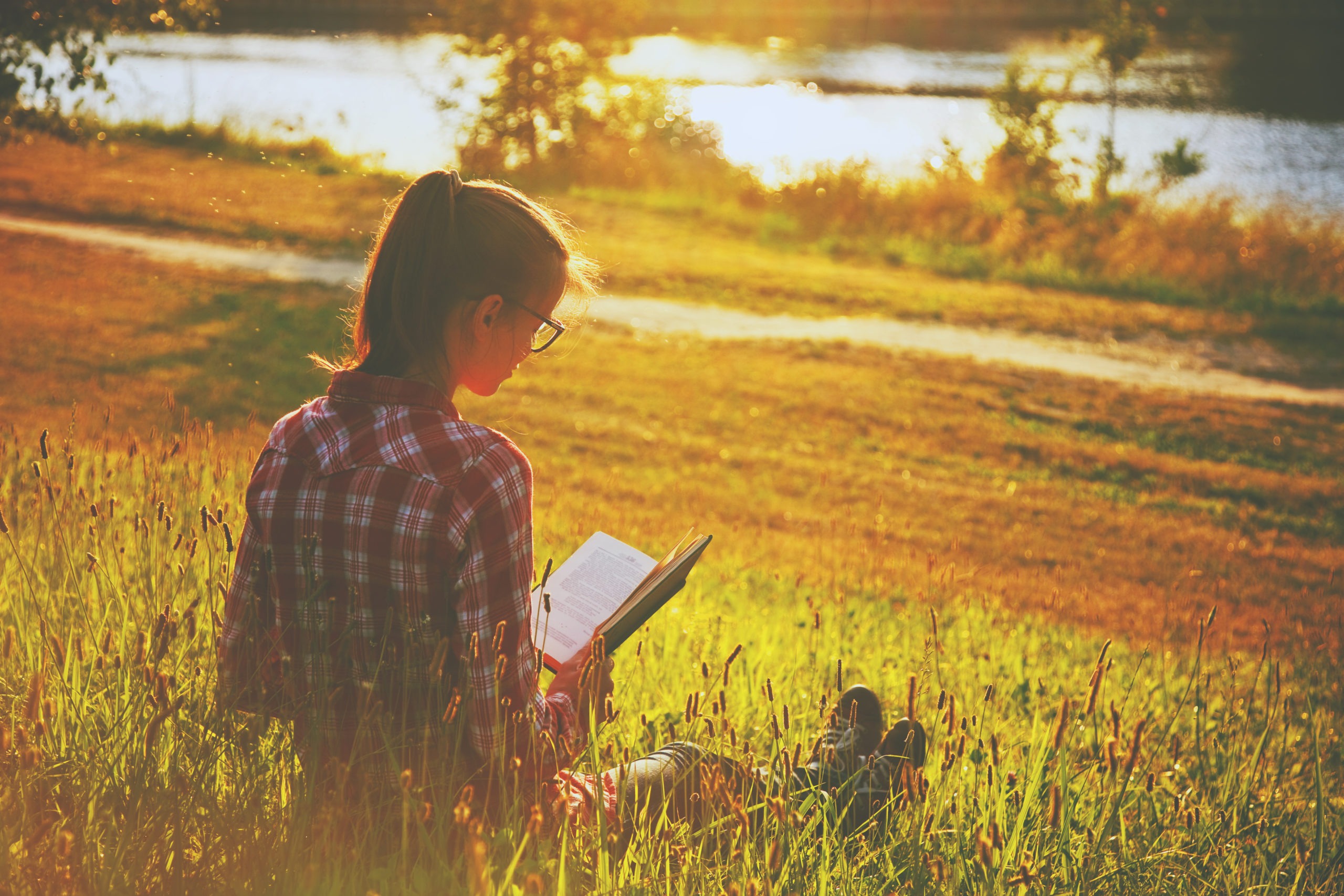 Girl reading a book on the grass by the river in summer.