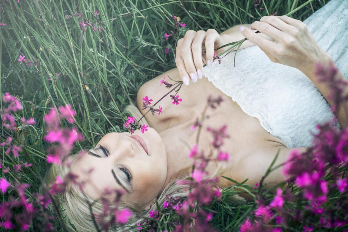 Beautiful young lady lying on the grass in the meadow and smelling pink flowers
