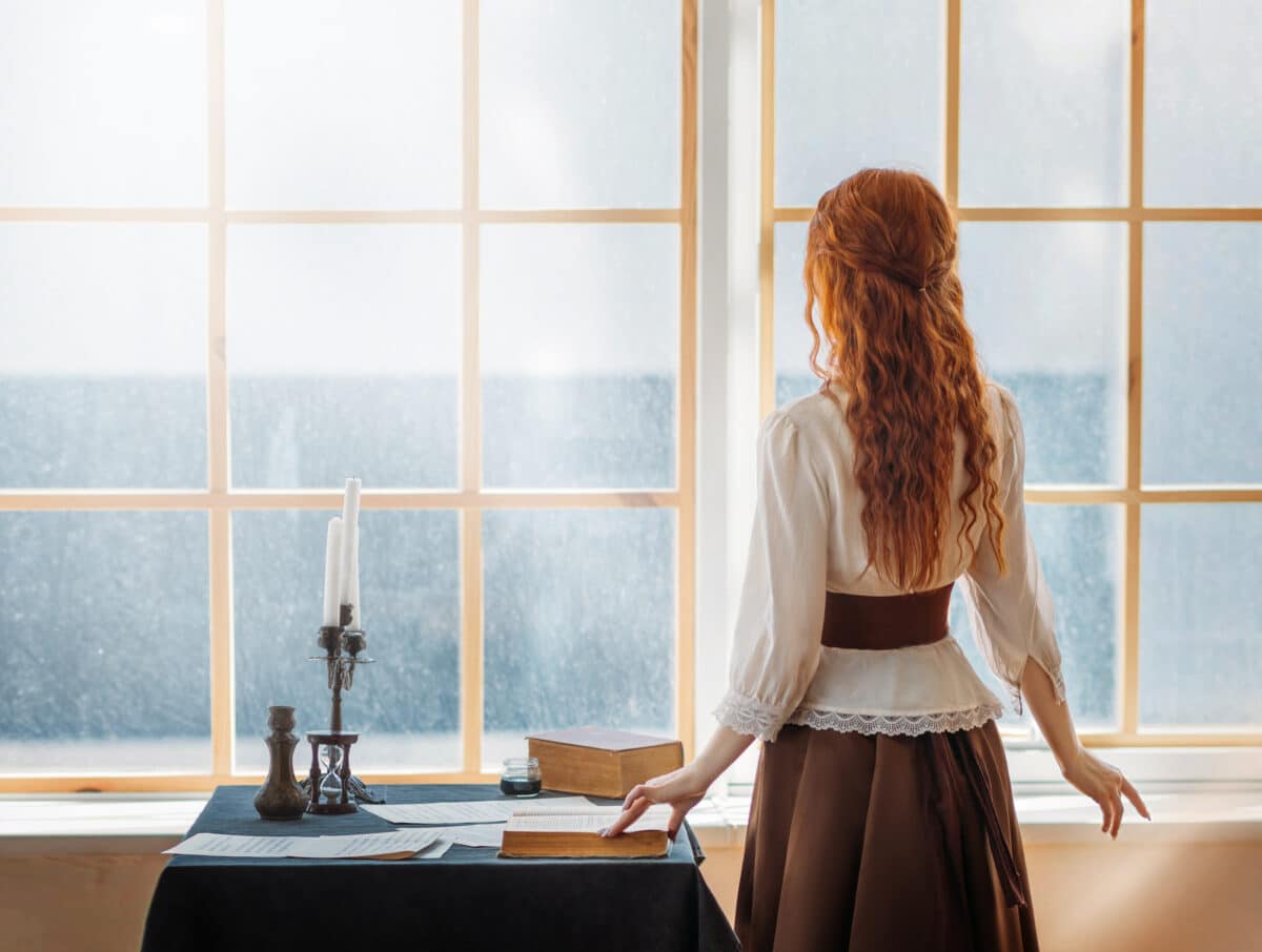 mysterious redhead woman stands in room near window waiting for love. Girl writer looking for inspiration. Long flowing red hair back rear view. lady queen vintage dress. royal cabinet old style room