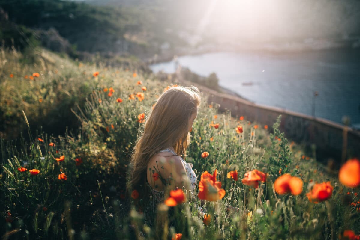 A young lady sitting among red poppies with the ocean view