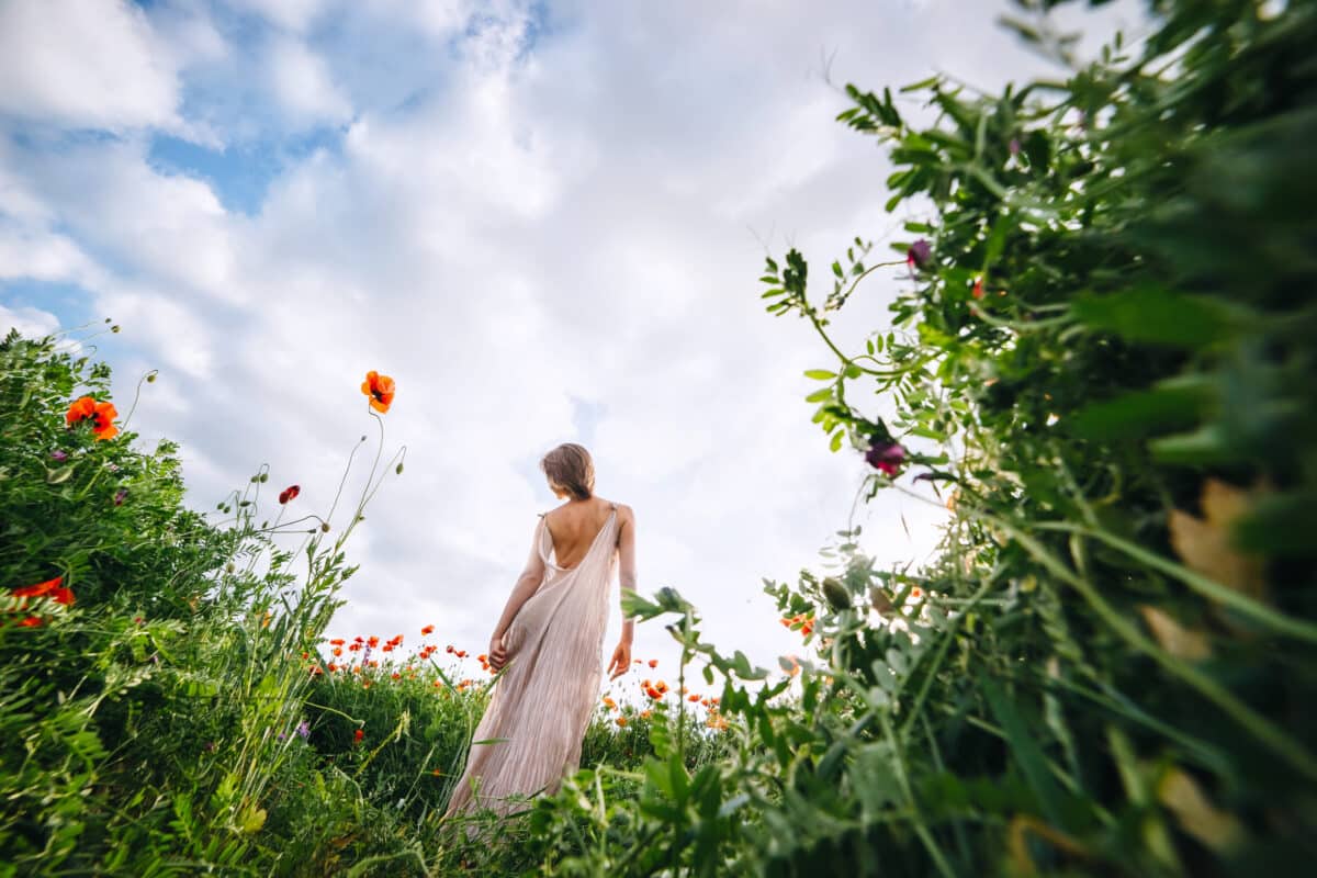 A beautiful woman in a white dress with short hair standing in the meadow with blooming poppies