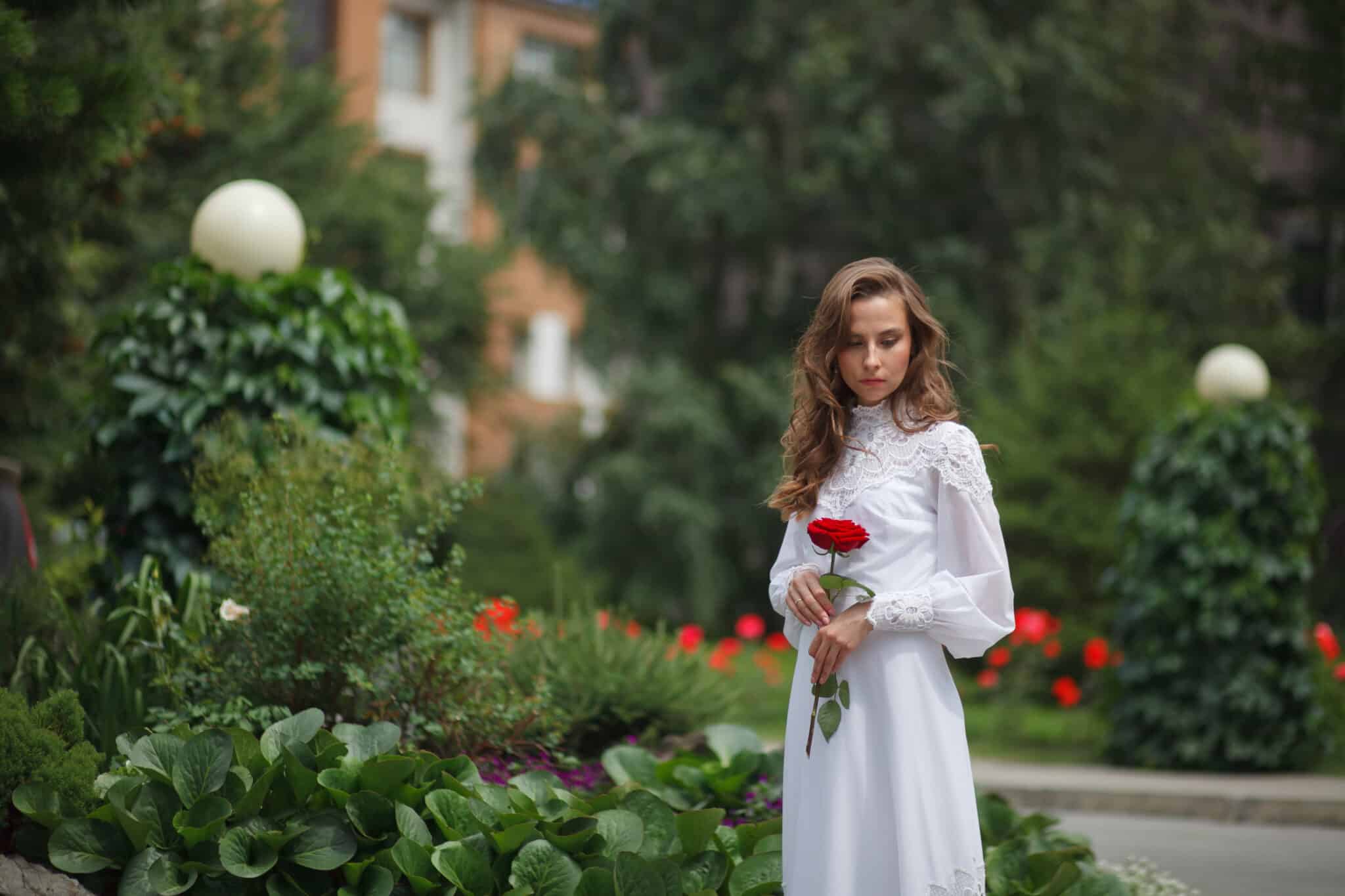 beautiful lady in a vintage dress walks in the garden holding a red rose

