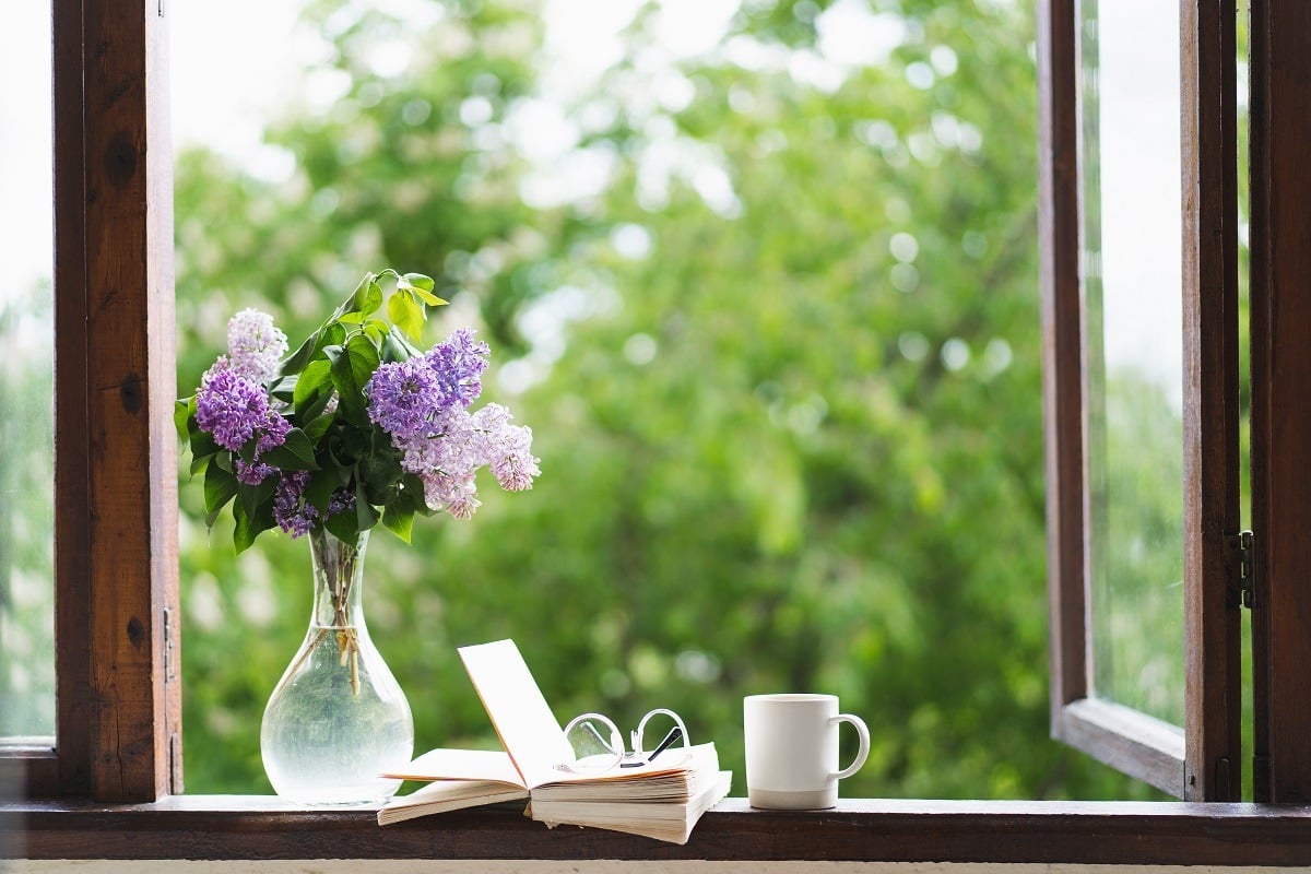 Book, glasses, cup of tea and lilac on a wooden window.