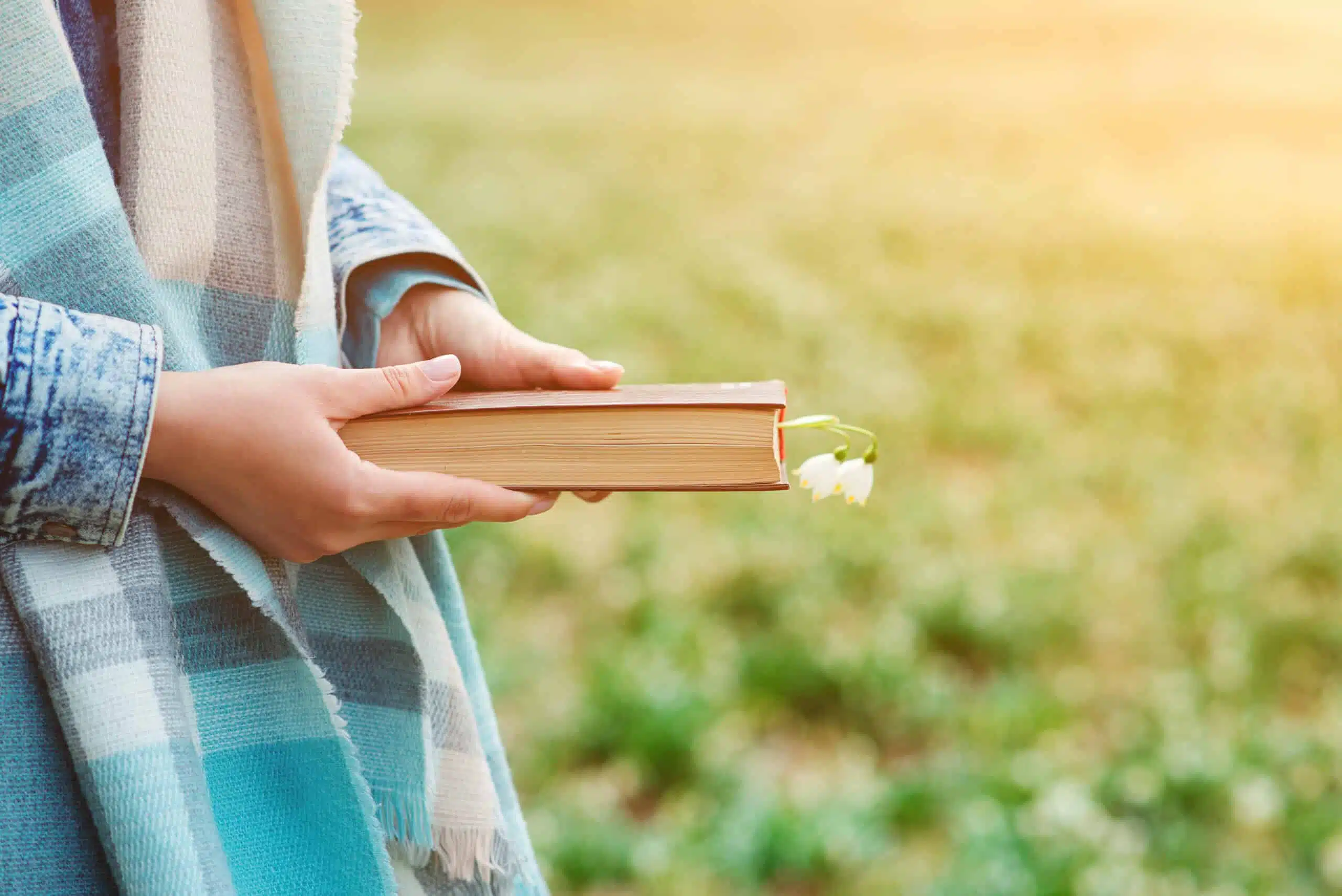 Woman holding a book, lilies of the valley inserted in between pages.