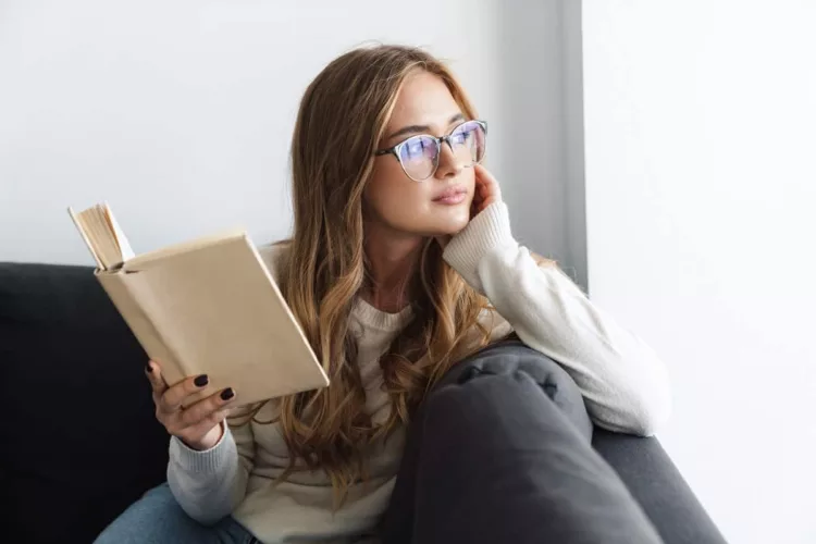 young serious woman reading book while sitting on couch