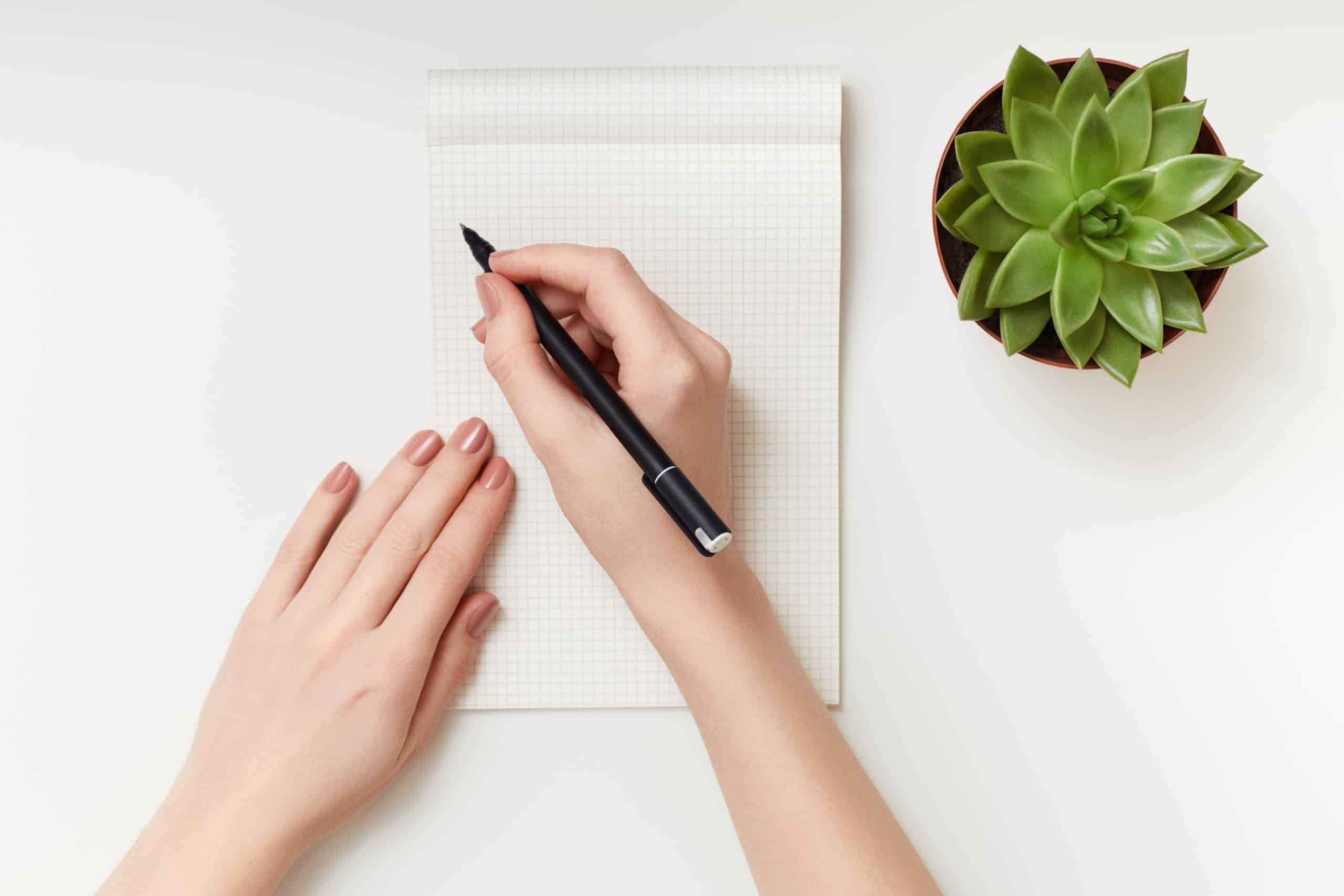 Woman's hands holding a pen over paper and a succulent plant