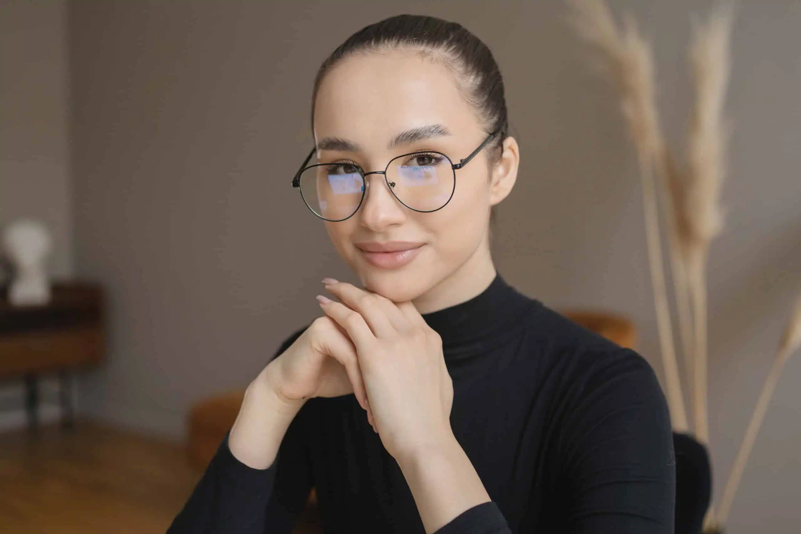 An attractive woman in black long sleeves wearing glasses sitting at her desk.