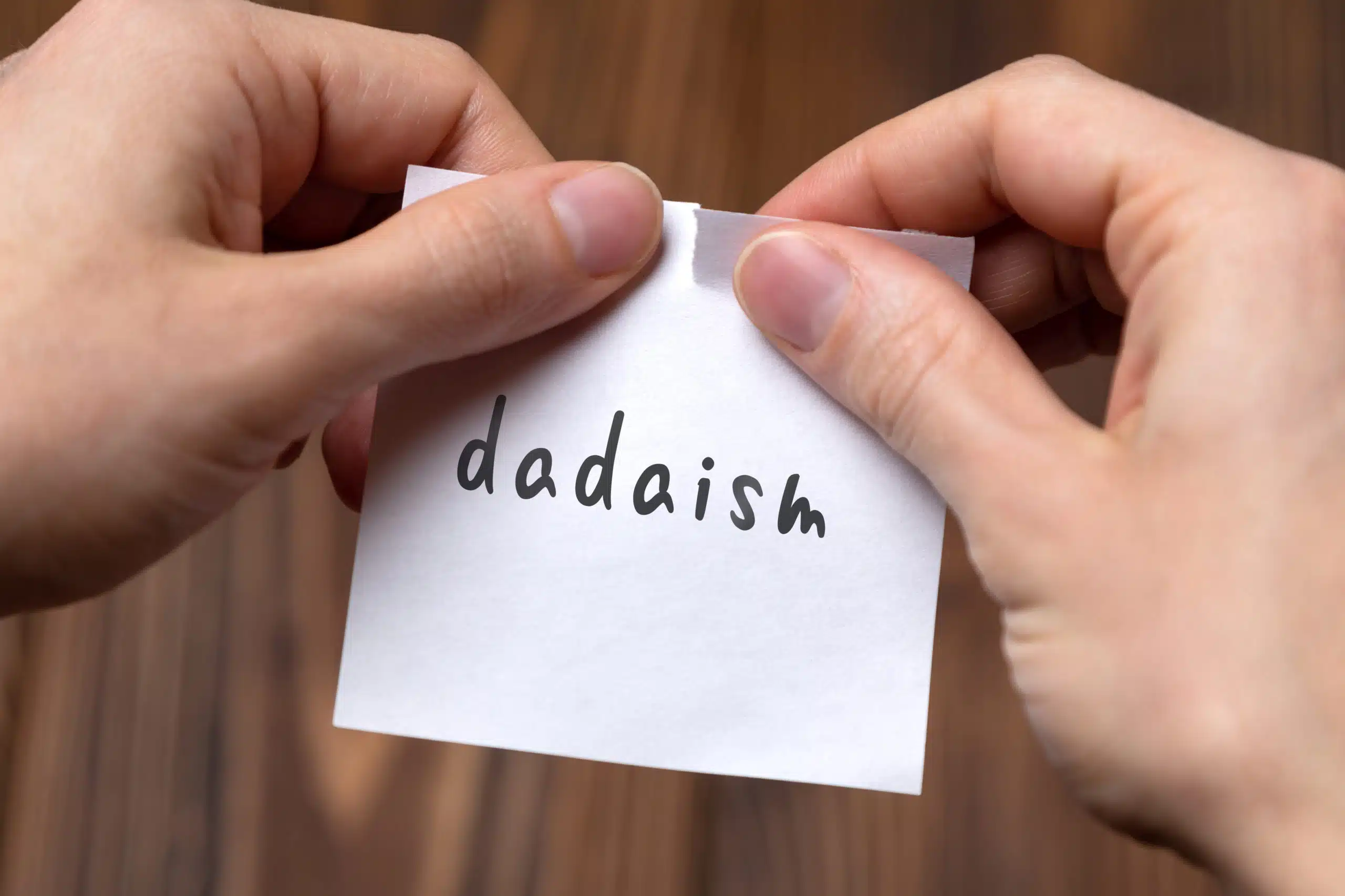 Hands tearing off paper with word dadaism