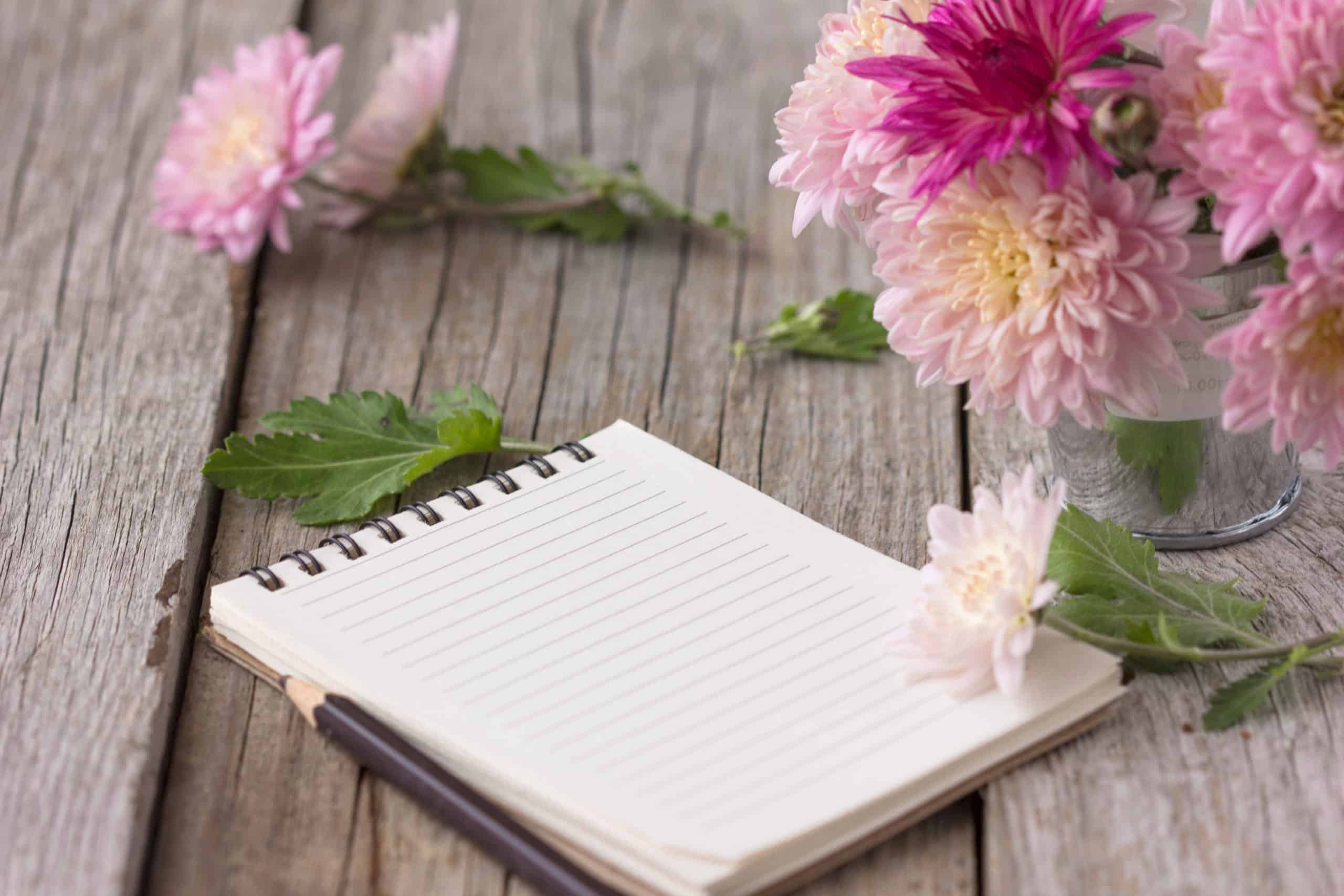 Open notebook with pen on a wooden desk with flowers.