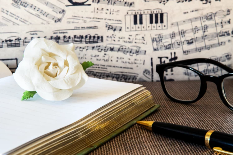 White paper rose on note book with black and gold pen against musical note paper