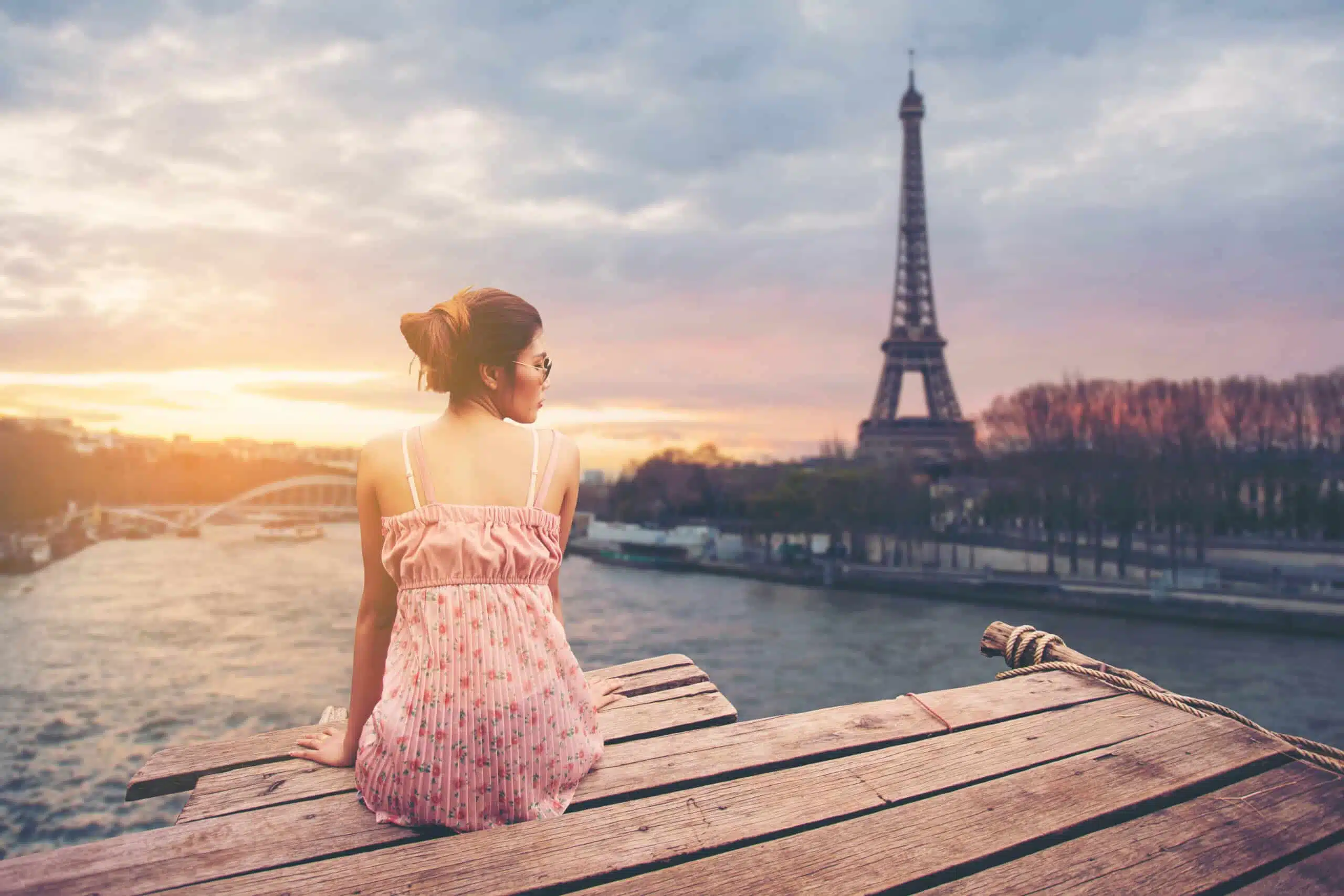 Young woman sitting on wood pier looking at Eiffel tower
