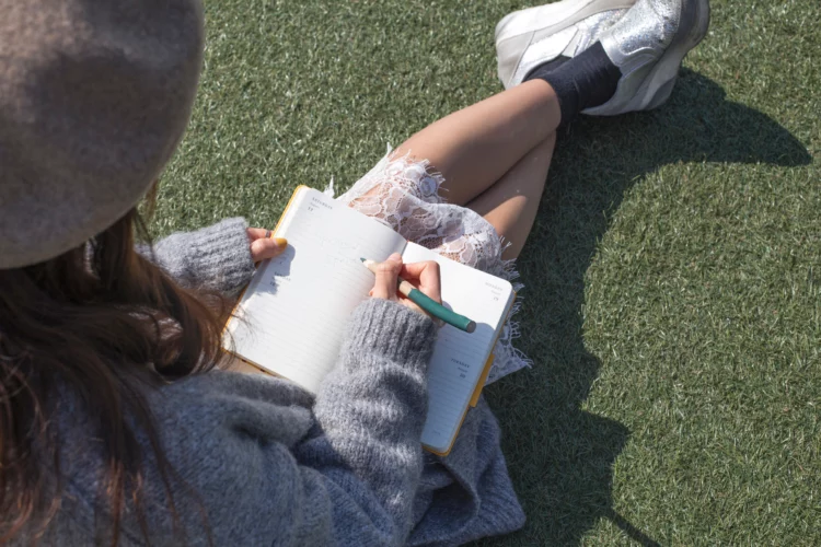 Woman writing on a blank notebook on grass outside