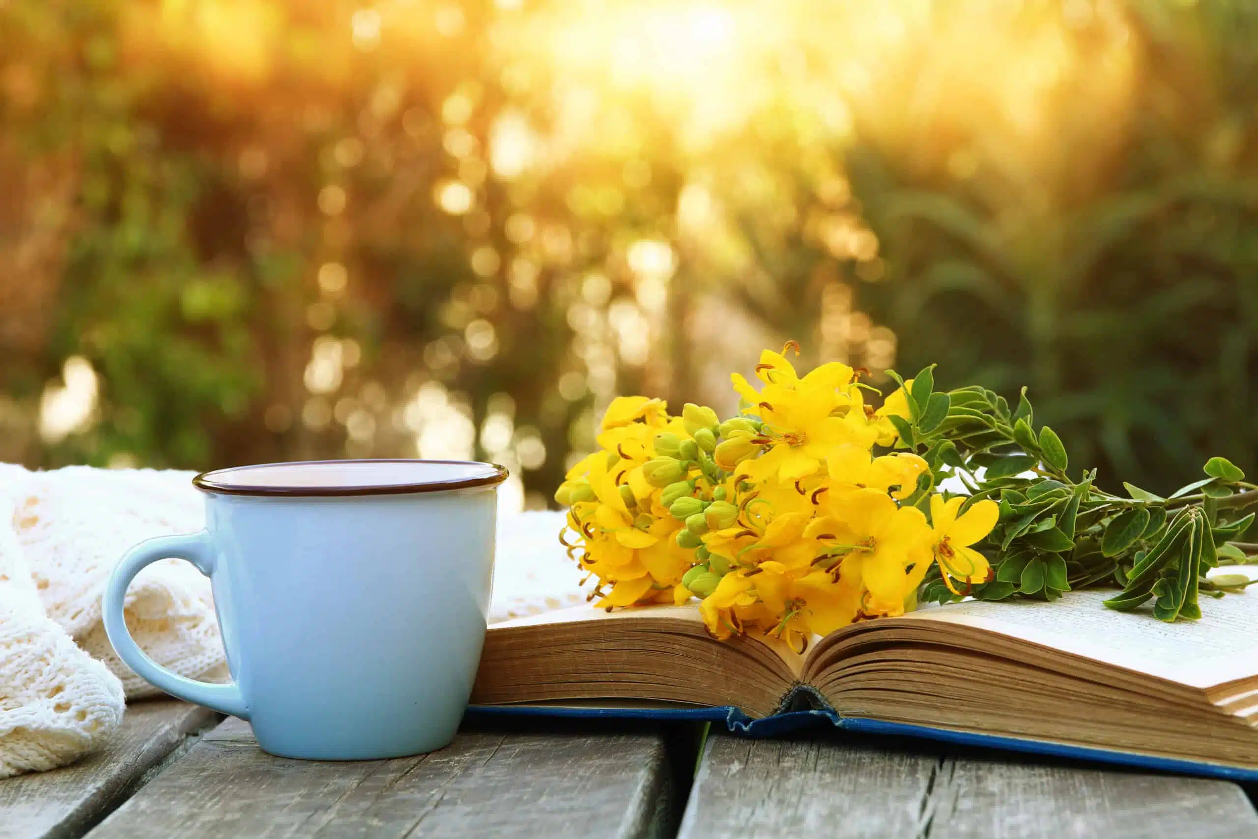 old book, cup of coffee next to a bouquet of yellow field flowers.