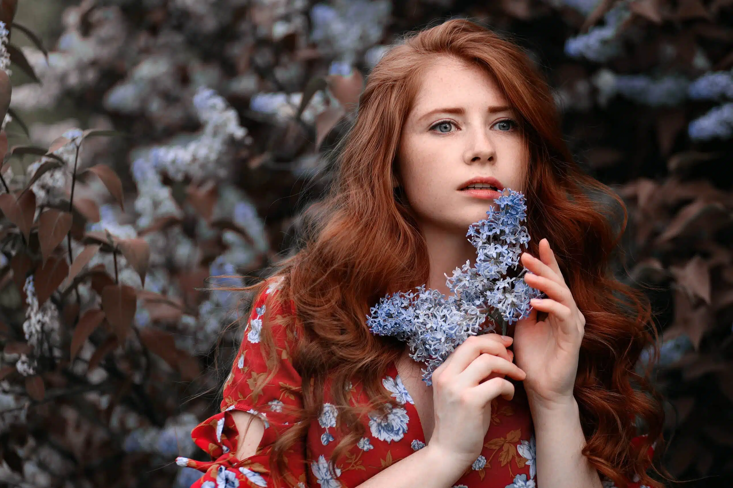 Young woman with long red hair in red dress holding lilac flower